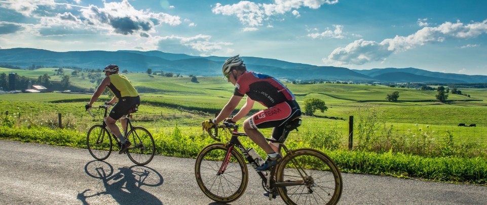 Two bicyclists dressed in gear pedal through the rolling green hills of Staunton Virginia. 