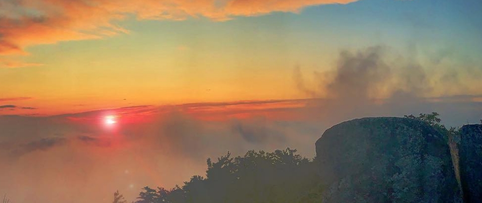 A vibrant orange and blue sunset over the mountains in Staunton Virginia is shaded by fog.