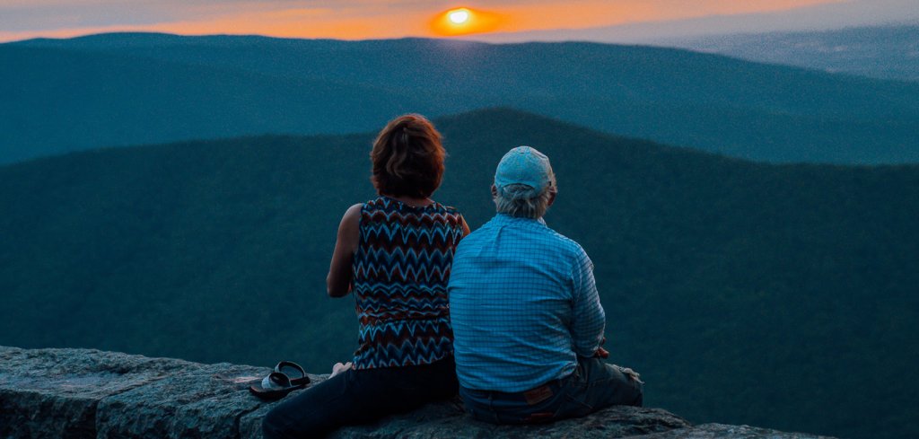 A man and women sitting on a ledge overlooking the mountains near staunton, va watching the sunset