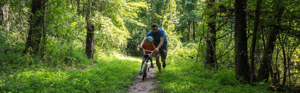 A father teaching his son how to ride a bike through the woods in staunton, va