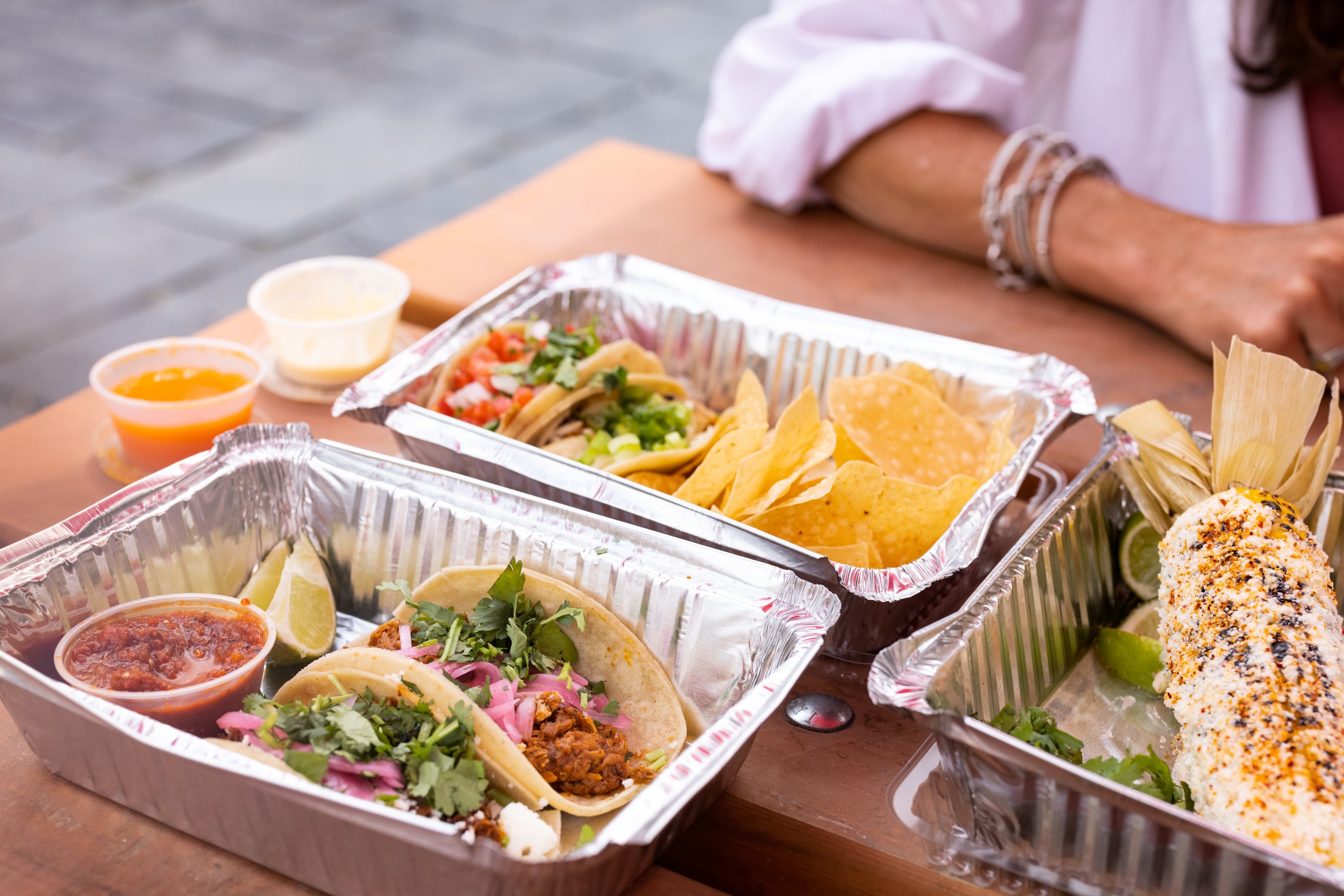 full trays of food show off mouthwatering tacos with salsa and lime, chips and dips, and Mexican street corn