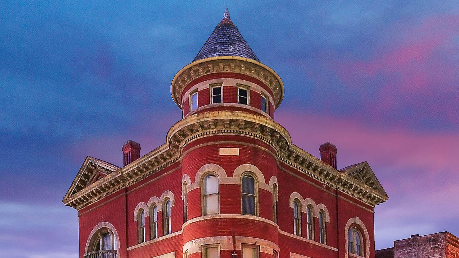 The red brick Marquis building in Staunton Virginia stands tall in the foreground of a blue and purple sky at dusk. 