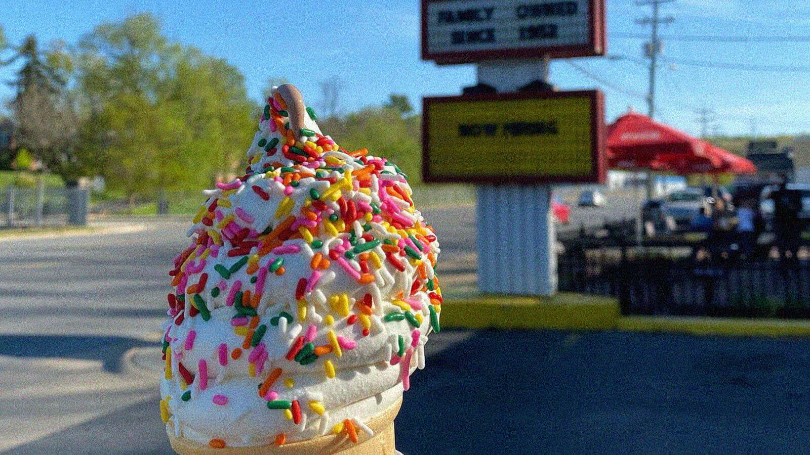 A vanilla ice cream cone is topped with sprinkles being held outside an ice cream parlor in Staunton Virgina. 
