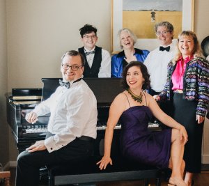 Staunton's Songs From the Stage event with pianist and vocalists sitting around a piano smiling