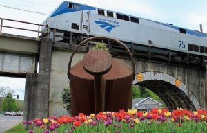 A train crosses a bridge adorned with colorful flowers, creating a beautiful scene of nature and transportation through Staunton, VA