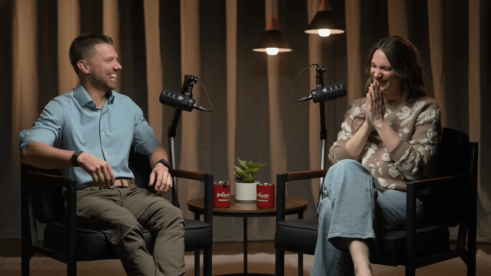 Peter And Samantha Laugh While Sitting Behind Podcast Microphones