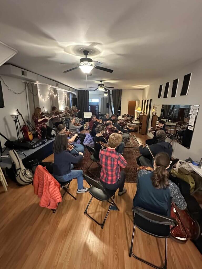 musicians gather around an instructor to play