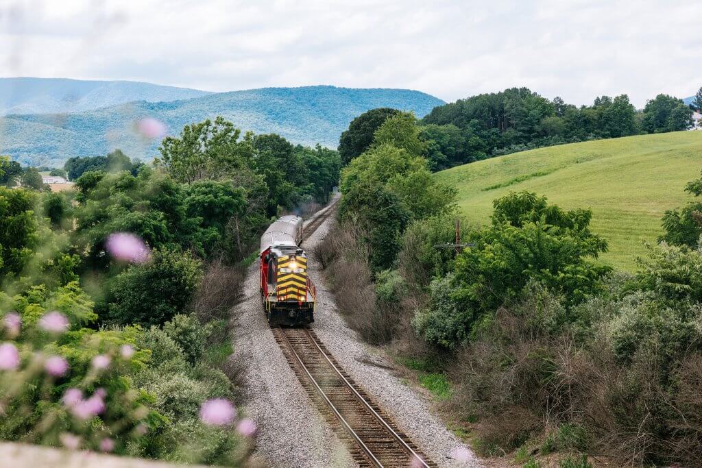 The engine and cars of the virginia scenic railway traveling on tracks through a hilly valley.