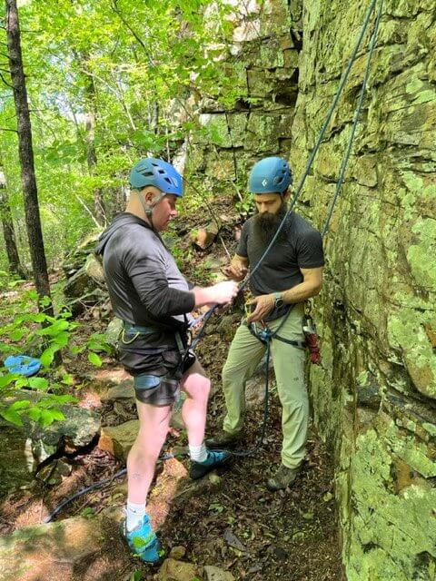 Instructor prepares man to rock climb with gear