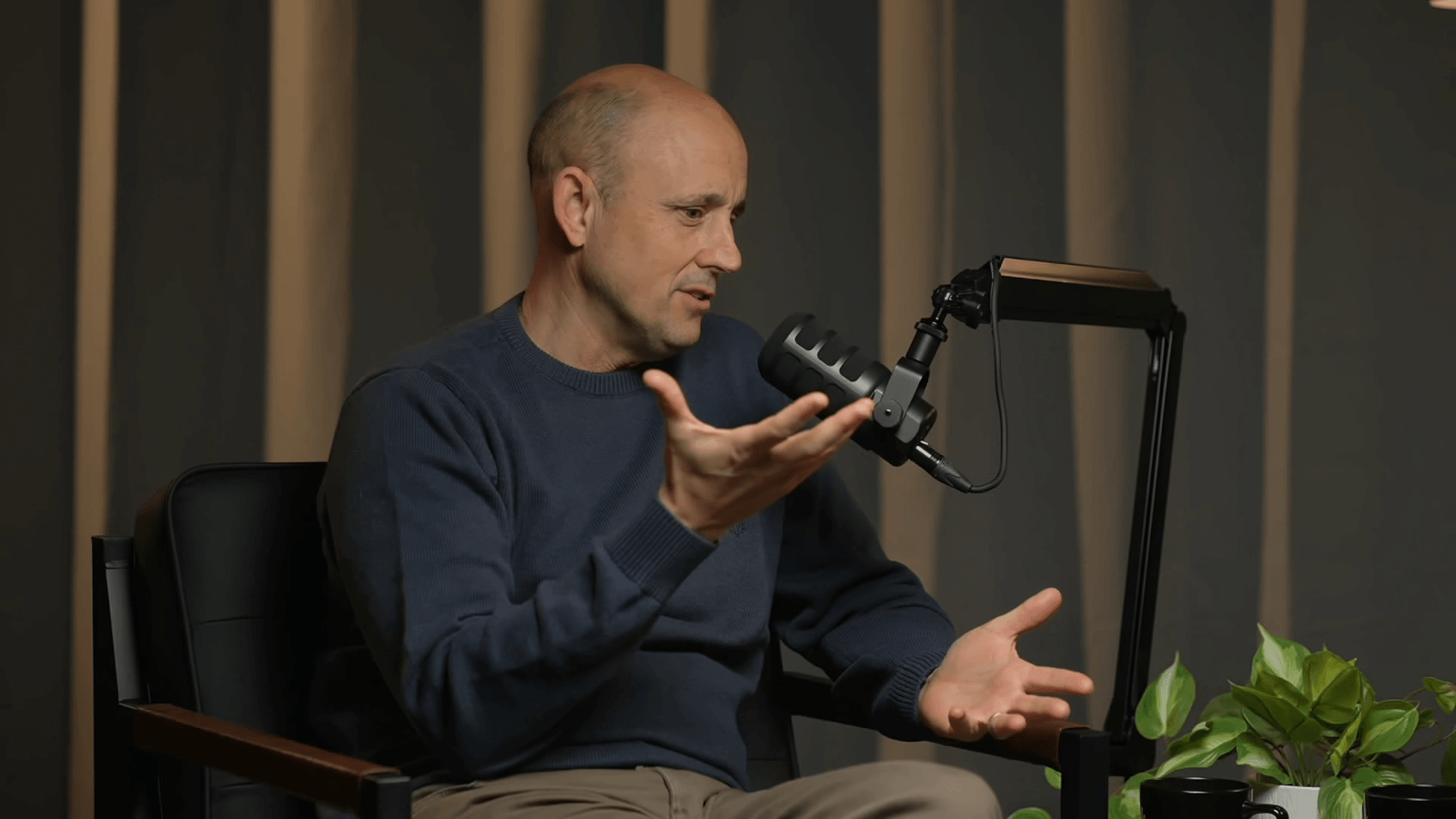 Jason sits behind a podcast mic with his right hand raised slightly higher than the left as if weighing two ideas