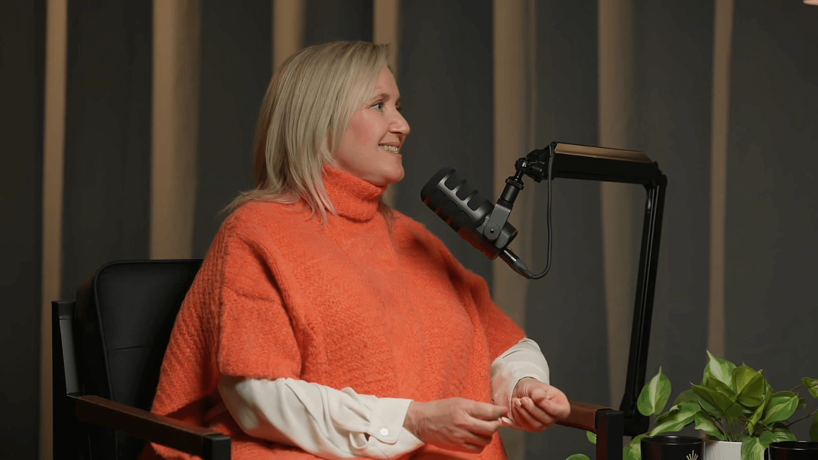 Robin von seldeneck sits behind a microphone wearing an orange and white sweater