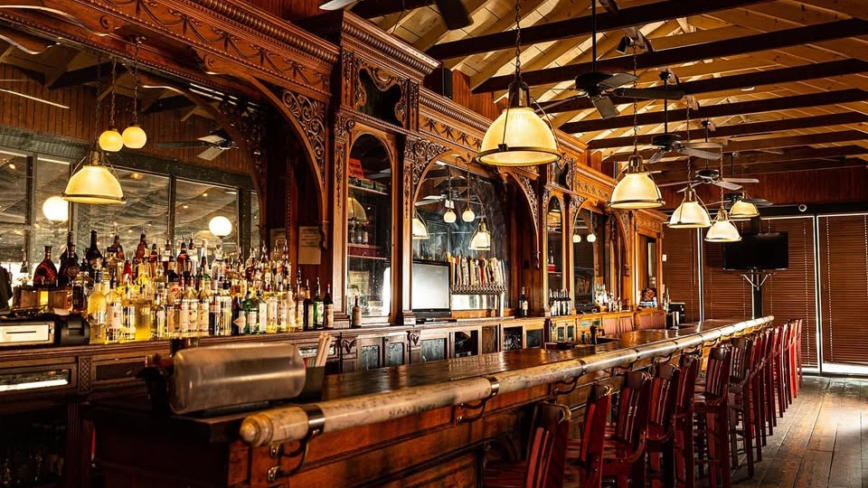 Classic wooden bar with ornate carvings, hanging lamps, and rows of liquor bottles
