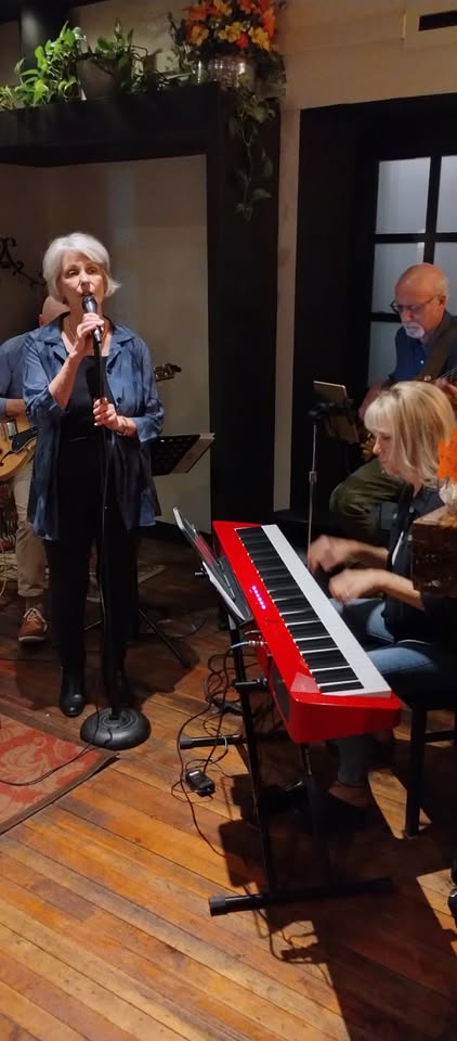 A woman sings into a microphone while a band plays, featuring a musician on a bright red keyboard