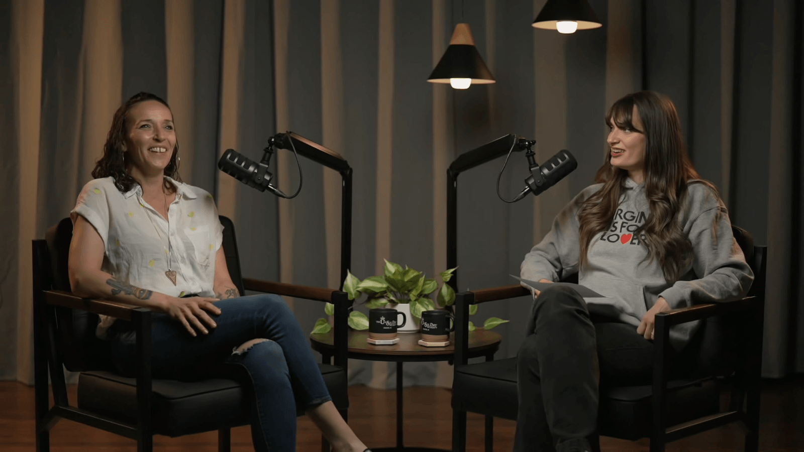 Laura and samantha talk behind podcast mics, smiling